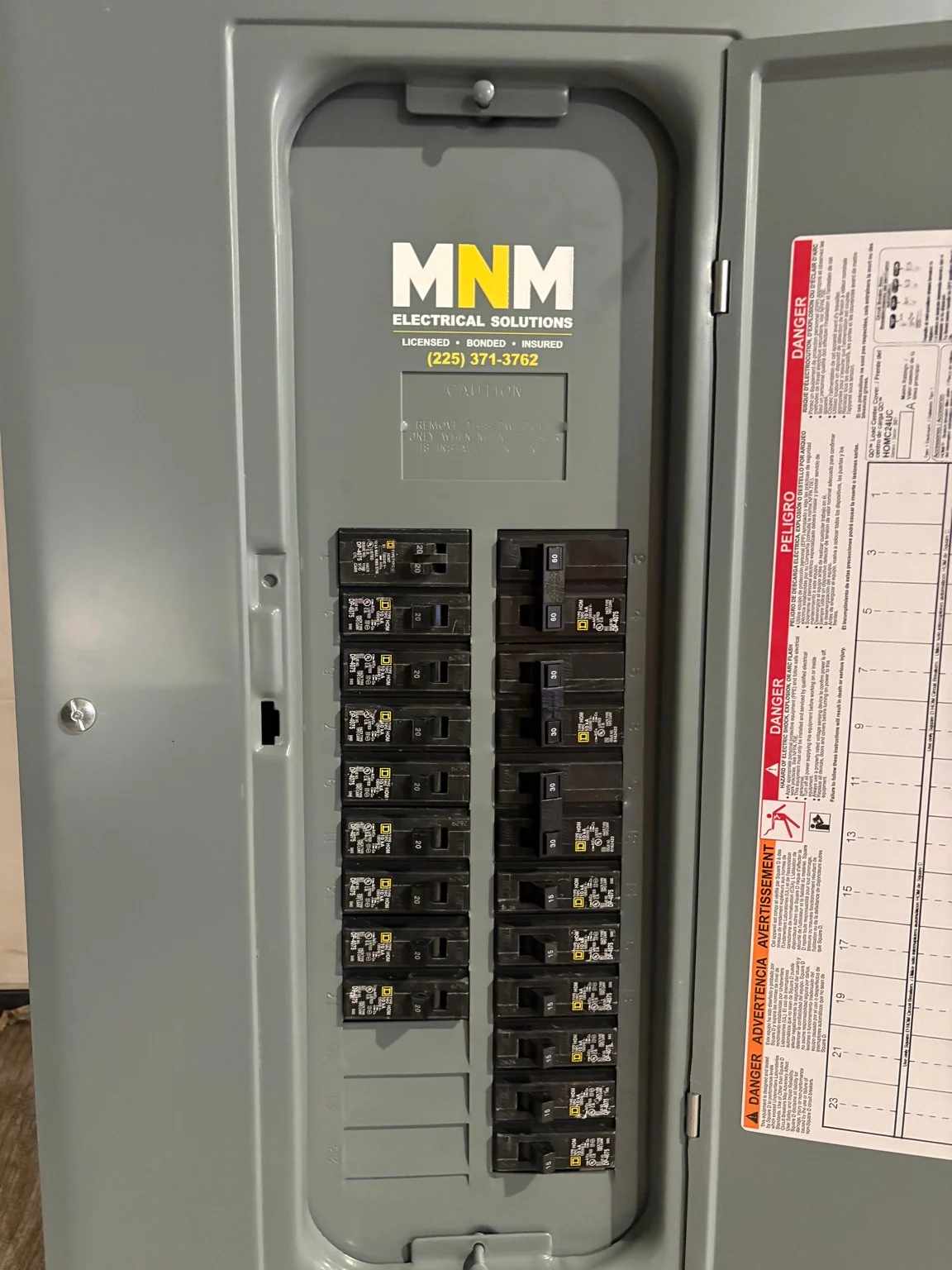 Electrical panel with circuit breakers and an MNM Electrical Solutions label